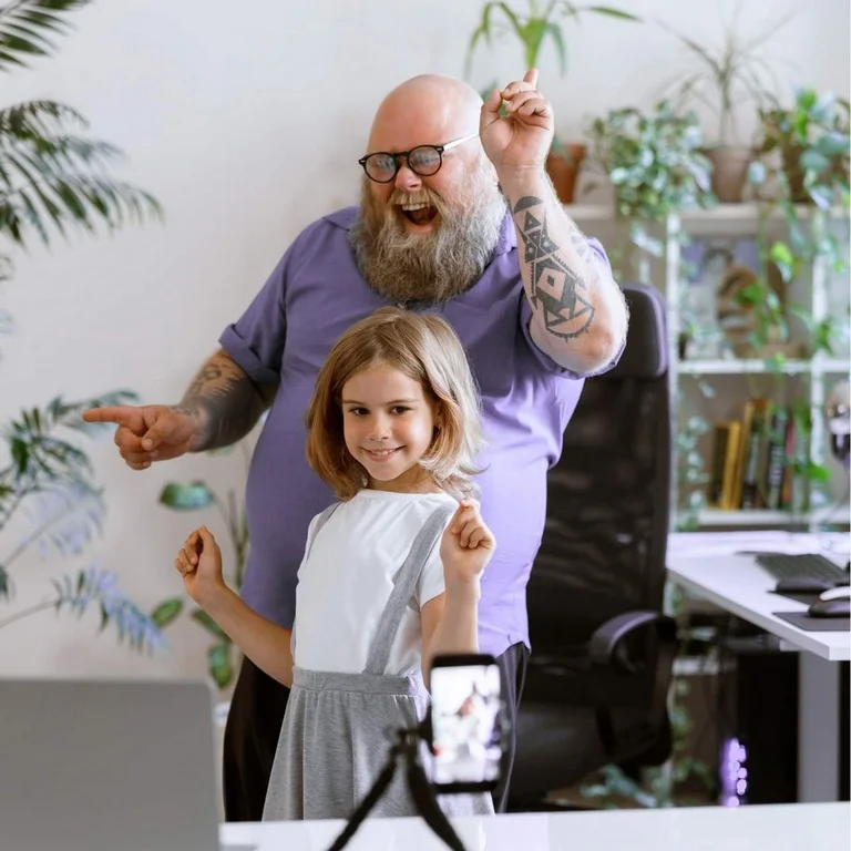 Un papa tatoué bedonnant s'amuse avec sa fille en prenant des photos de leur chorégraphie.