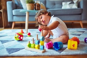 Un enfant joue avec des blocs de bois sur un tapis.