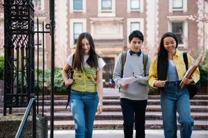 Trois jeunes étudiants qui marchent sur le campus universitaire avec des sacs à dos et des livres en main.