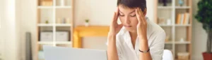 Une femme stressée devant son ordinateur qui se masse les tempes.