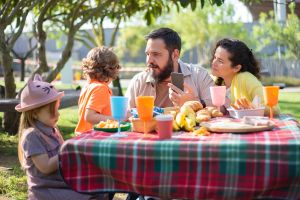 Une famille qui pique-nique à l'extérieur. Les parents écoutent activement leurs enfants autour de la table.