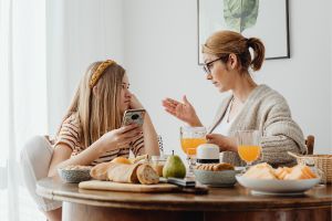 Communication parent-enfants interrompue par les téléphones : une fille est sur son smartphone à table avec sa mère.