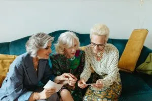 Trois femmes seniors qui cohabitent et regardent un téléphone en souriant.