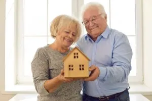 Un couple de seniors qui tiennent une maison en bois dans leurs mains.