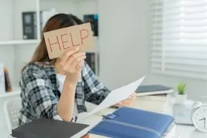 Stress et perdre du poids : une jeune femme qui étudie avec un petit carton où il est marqué "help" (à l'aide).