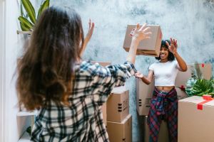 Deux jeunes femmes qui emménagent dans leur logement étudiant en colocation. Elles portent des cartons.