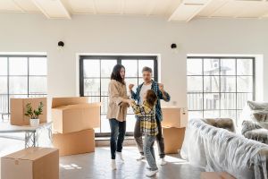 Une famille heureuse d'emménager grâce aux aides au logement. Ils dansent dans un salon entourés de cartons.