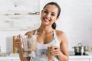 Une femme qui boit un smoothie à base de maca en souriant.