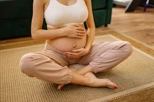 Probiotiques et femmes enceintes : une femme enceinte qui tient son ventre en main, assise par terre sur un tapis.