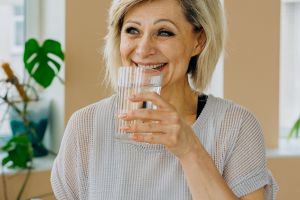 Une femme d'âge mûr boit un verre d'eau car l'hydratation est essentielle pour bien vieillir.