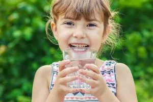 Une jeune fille boit un verre d'eau en souriant.