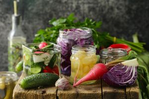 Aliments lacto-fermentés riches en probiotiques pour améliorer la digestion. Des bocaux en verre remplis de légumes sont sur une table en bois.