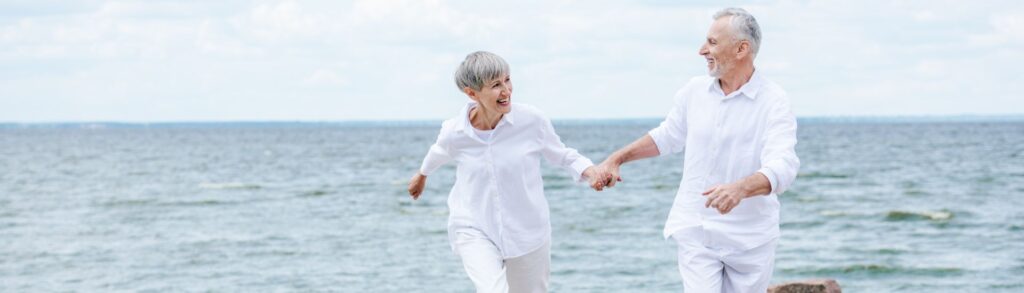 Un couple à la retraite qui court sur une plage heureux.