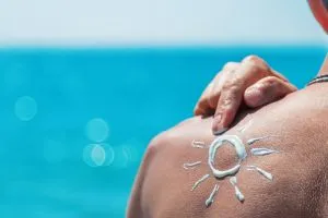 Un homme qui bronze en face de la mer. Il a un soleil dessiné en crème solaire sur l'épaule.