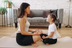 Une maman et sa fille qui font du yoga assises par terre en routine matinale.