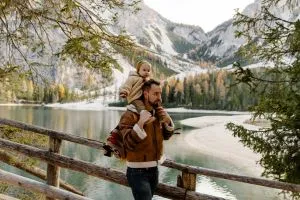 Un jeune père célibataire qui profite du CMG. Il se balade en forêt devant un lac avec son enfant sur le dos.