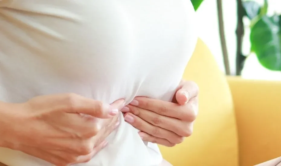 Une femme qui se tient l'abdomen avec ses deux mains en signe de douleurs à la vésicule biliaire.