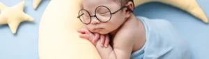 Nourrisson et sommeil : un bébé dort sur un doudou en forme de lune.