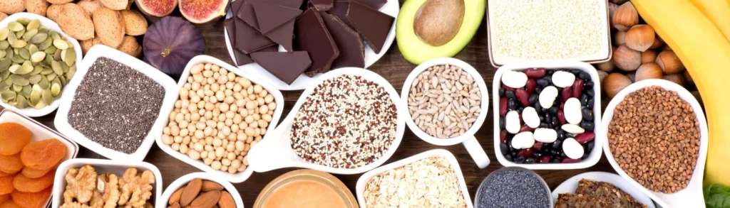Aliments riches en magnésium (avocat, chocolat noir, graines, oléagineux, etc.) sur une table en bois.