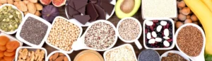 Aliments riches en magnésium (avocat, chocolat noir, graines, oléagineux, etc.) sur une table en bois.