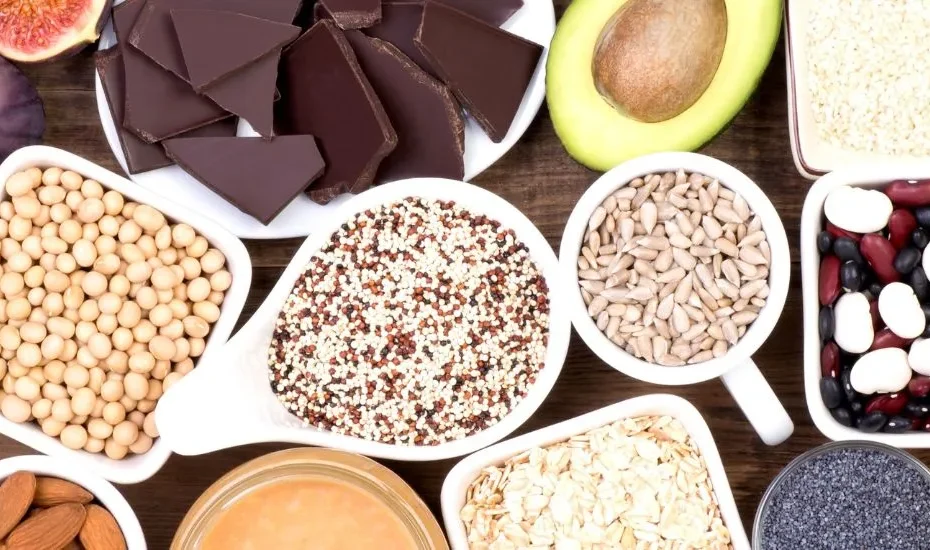 Aliments riches en magnésium (avocat, chocolat noir, graines, oléagineux, etc.) sur une table en bois.