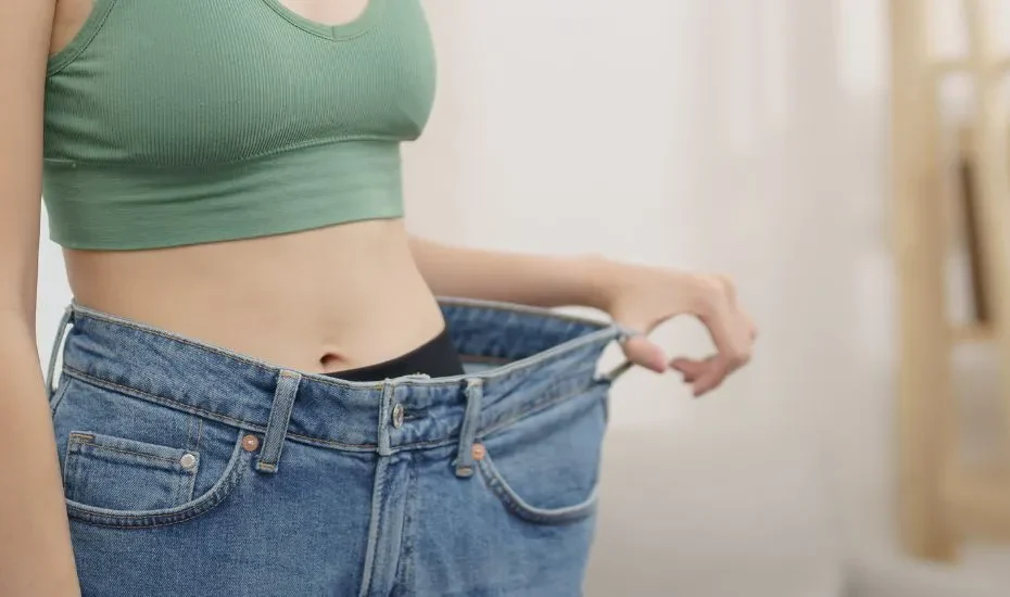 Une femme mince dans un pantalon en jeans trop grand. Elle a réussi à perdre du poids en relançant son métabolisme lent.