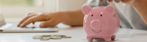 Budget familial : une maman met une pièce dans une tirelire en forme de cochon rose.