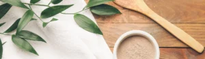 De la poudre de PQQ (Pyrroloquinoléine quinone) sur une table en bois. Il y a des feuilles vertes à côté.