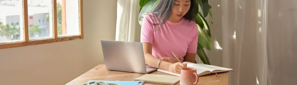 Une jeune femme asiatique cherche un stage étudiant en ligne. Elle écrit des choses devant son ordinateur.