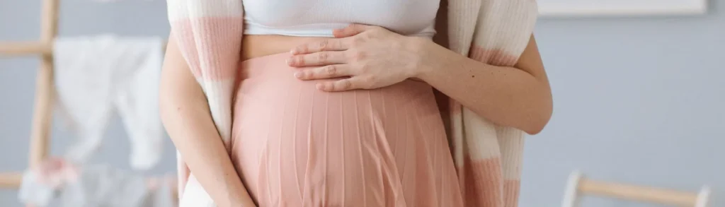 Une femme enceinte pose ses mains sur son ventre au troisième trimestre de grossesse.