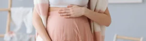 Une femme enceinte pose ses mains sur son ventre au troisième trimestre de grossesse.