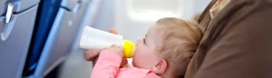 Un père qui va voyager avec son bébé en avion. Il lui donne le biberon sur ses genoux dans un avion.