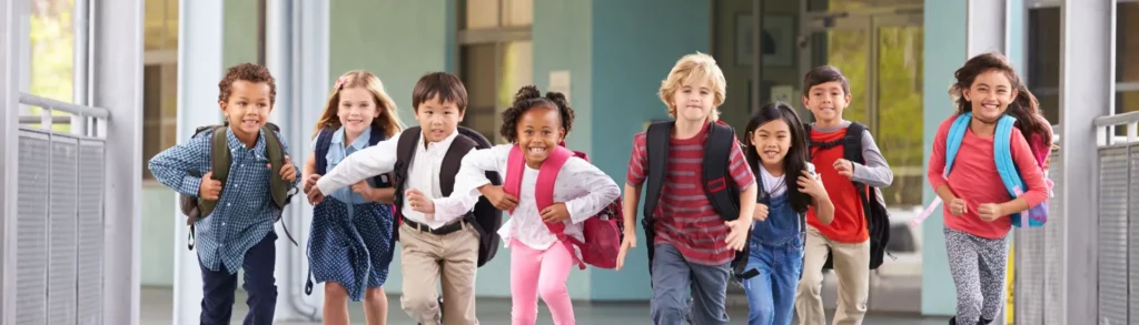 Des enfants qui courent à la sortie de l'école. Ils ont une assurance scolaire et sourient.