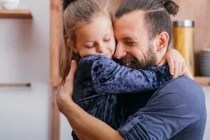 Un papa fait un câlin en souriant à sa fille. 