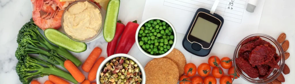 Aliments IG bas sur une table à côté d'un appareil pour mesurer a glycémie. Il y a des légumes, des légumineuses, des crevettes.