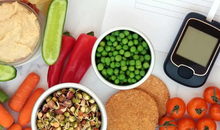 Aliments IG bas sur une table à côté d'un appareil pour mesurer a glycémie. Il y a des légumes, des légumineuses, des crevettes.