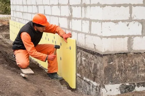 Un ouvrier met en place l'isolation thermique des murs d'une maison grâce aux aides à la rénovation énergétique.