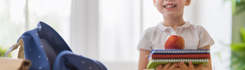 Une enfant qui tient des livres pour la rentrée scolaire et un pomme pour l'immunité.