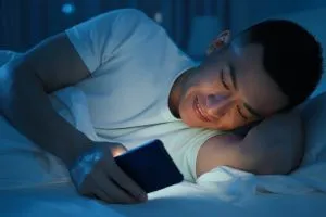 Un jeune étudiant en manque de sommeil qui regarde son téléphone dans son lit.