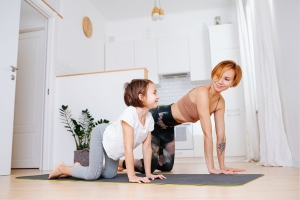 Une maman et sa fille font des exercices de stretching dans le cadre d'une routine bien-être. Elles sont à 4 pattes sur un tapis.