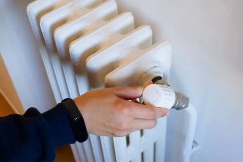 Une main qui baisse le radiateur pour réduire sa facture d'électricité.