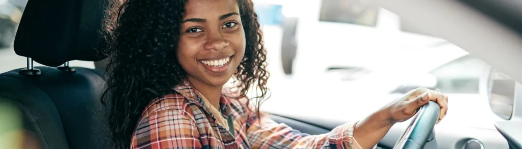 Assurance auto jeune conducteur : une jeune femme sourit au volant de sa voiture.