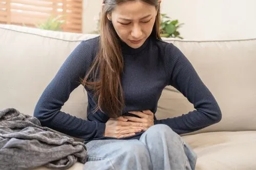 Une femme qui se tient le ventre en signe de douleurs digestives. Elle est assise sur un canapé.