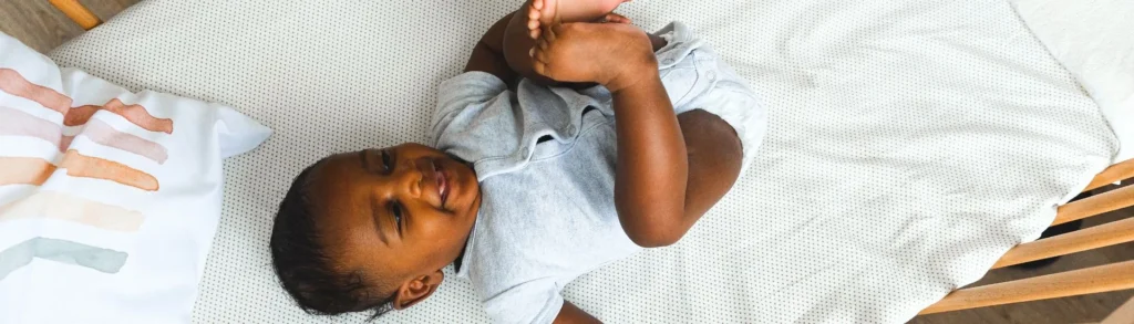 Un bébé dans un lit qui sourit en jouant avec ses pieds. Ses parents ont demandé les aides financières en 2026.