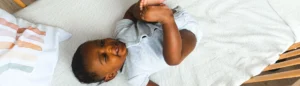 Un bébé dans un lit qui sourit en jouant avec ses pieds. Ses parents ont demandé les aides financières en 2026.