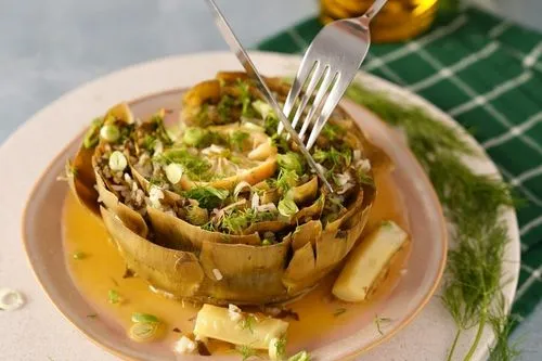 Artichaut cuit riche en bienfaits. Une fourchette et un couteau coupent un morceau d'artichaut farci.