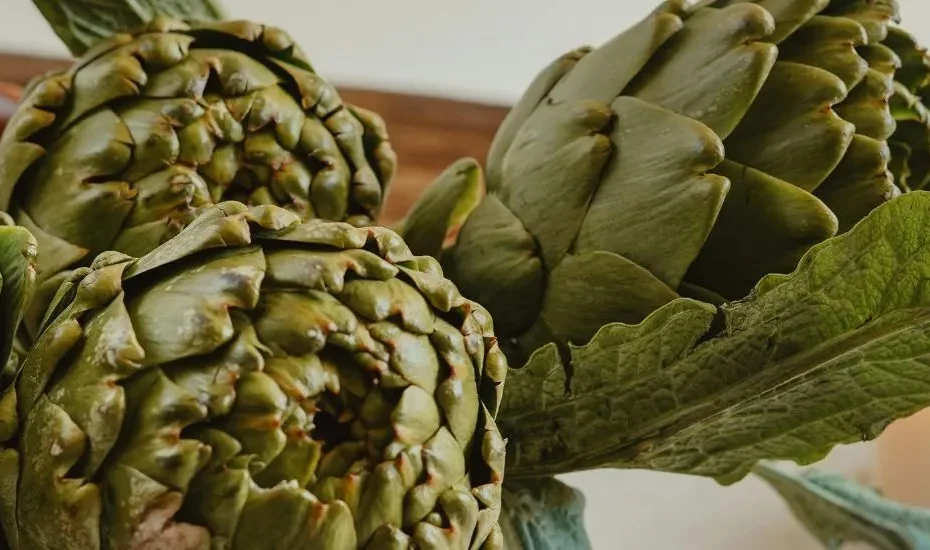 Des artichauts riches en bienfaits posés dans un panier à côté d'une bougie.
