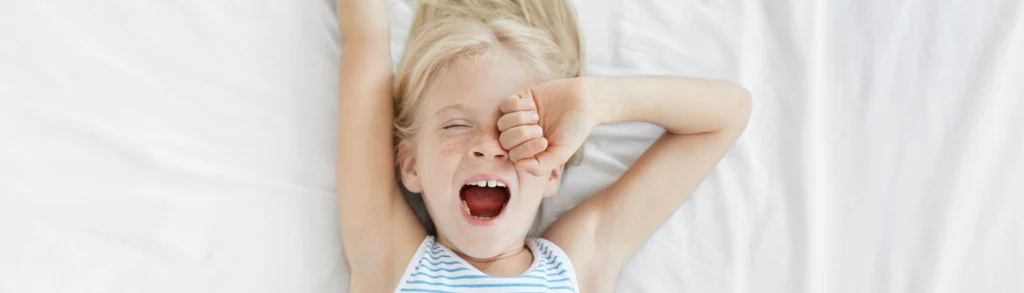 Une enfant dans son lit est fatiguée, elle baille et s'étire.
