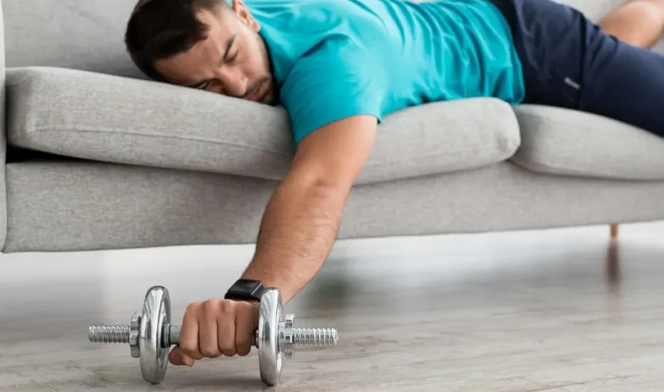Un homme couché sur un canapé avec un haltère en main, en signe de récupération musculaire.