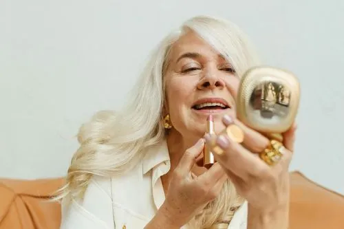 Une belle femme âgée qui se maquille avec le sourire, en pleine forme.